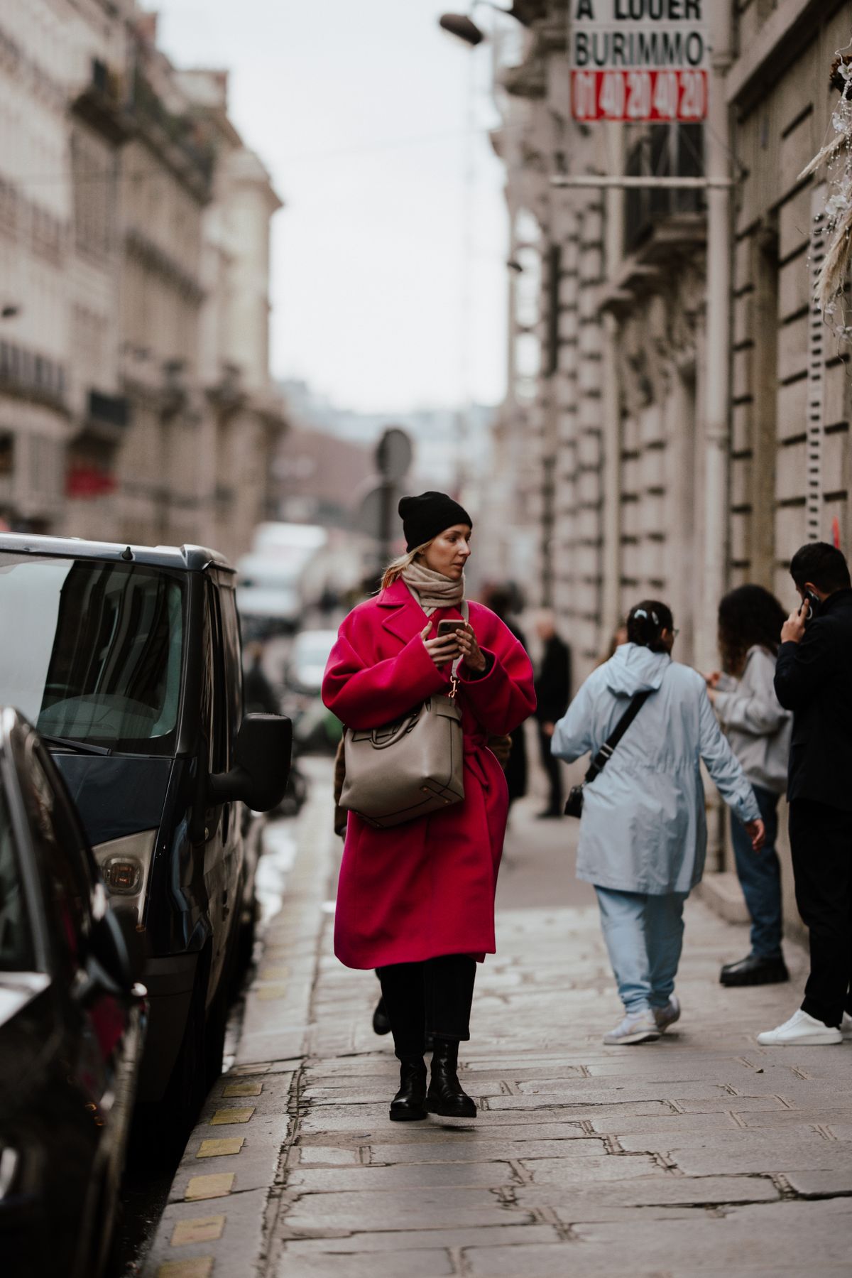 A woman in a vivid red coat crossing a busy autumn street.