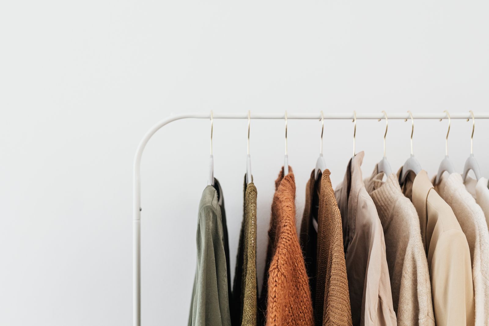 A rail of neutral-toned knits and coats on wooden hangers.