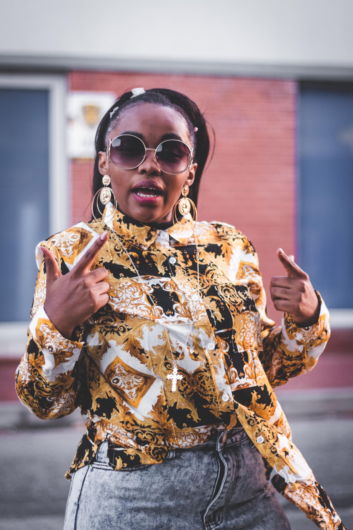 A woman in a bold printed jacket and sunglasses posing outdoors.